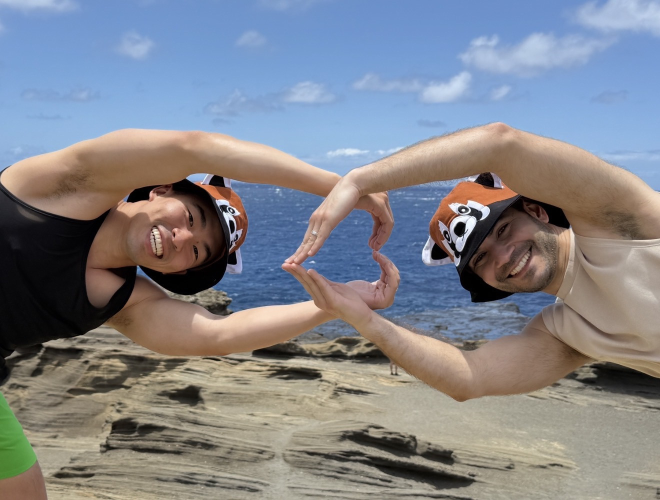 Jonathan and Frank making a heart shape with their arms on a beach